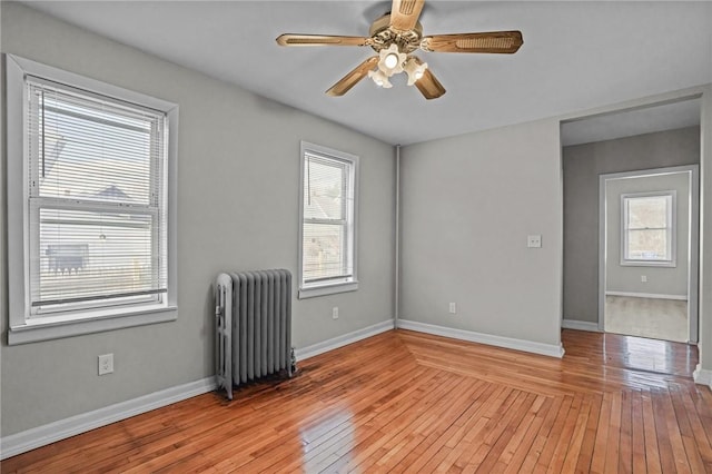 empty room featuring radiator heating unit, ceiling fan, and light hardwood / wood-style flooring