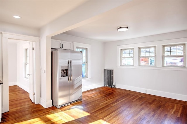 kitchen with radiator, hardwood / wood-style floors, white cabinets, and stainless steel fridge with ice dispenser