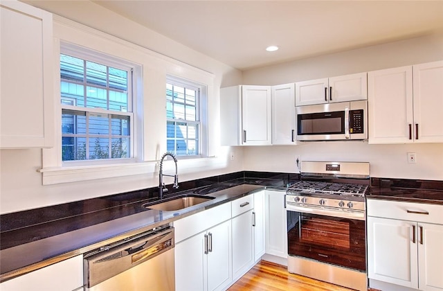 kitchen with white cabinetry, appliances with stainless steel finishes, sink, and dark stone countertops