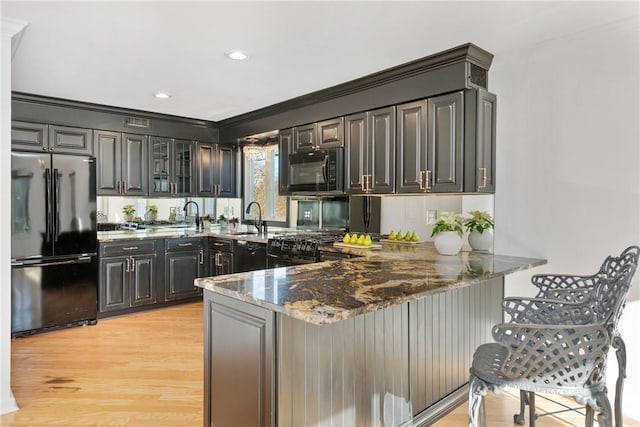 kitchen featuring dark stone countertops, sink, kitchen peninsula, and black appliances