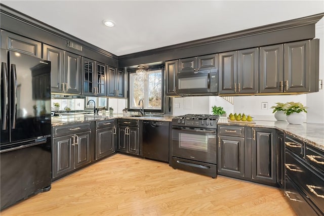 kitchen featuring sink, ornamental molding, light stone counters, black appliances, and light wood-type flooring