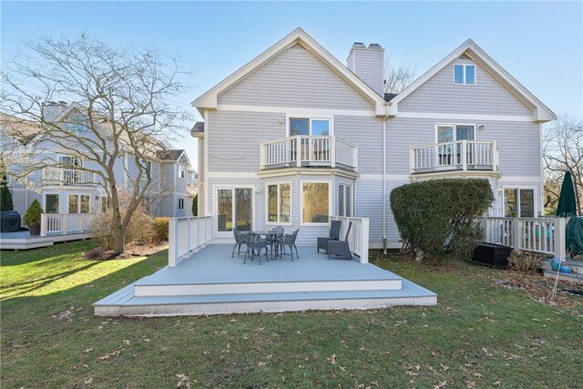 rear view of house with a wooden deck, a balcony, and a lawn