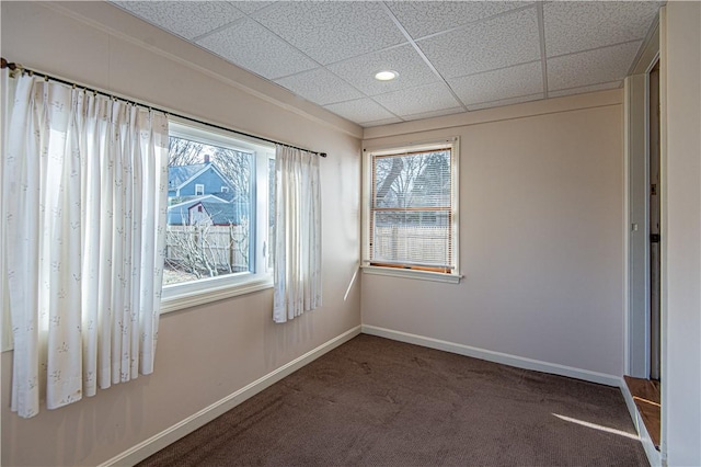 unfurnished room featuring dark colored carpet and a drop ceiling