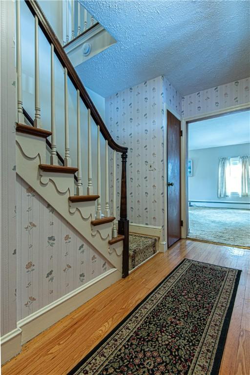 stairs featuring hardwood / wood-style floors, a baseboard radiator, and a textured ceiling