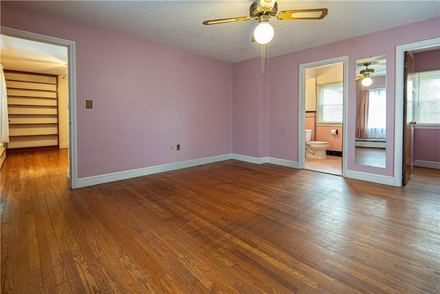 unfurnished bedroom featuring connected bathroom, hardwood / wood-style floors, a spacious closet, baseboard heating, and a textured ceiling