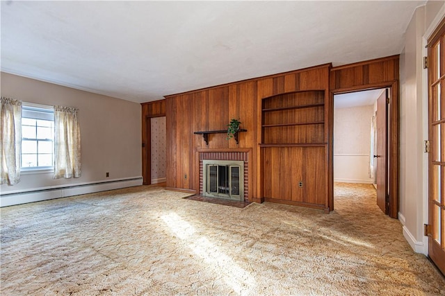 unfurnished living room with built in shelves, wood walls, baseboard heating, ornamental molding, and a fireplace