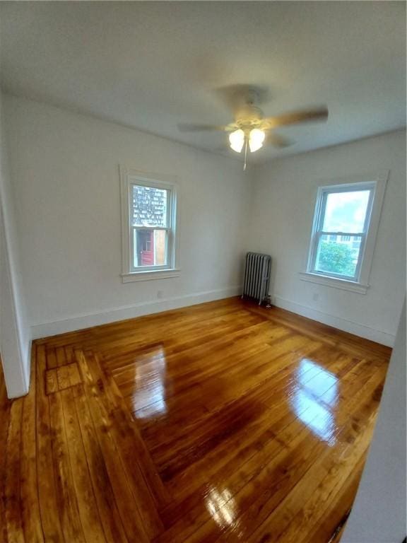 spare room featuring radiator, hardwood / wood-style flooring, plenty of natural light, and ceiling fan