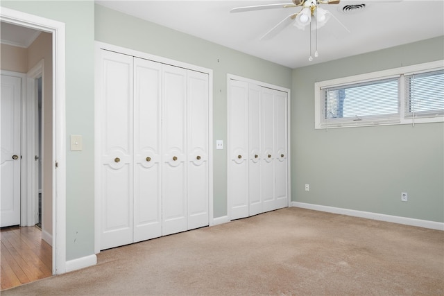 unfurnished bedroom featuring two closets, light colored carpet, and ceiling fan