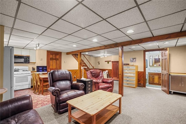 carpeted living room featuring a drop ceiling and wood walls