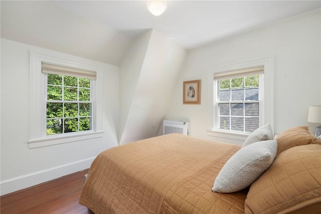 bedroom with dark wood-type flooring, vaulted ceiling, multiple windows, and an AC wall unit