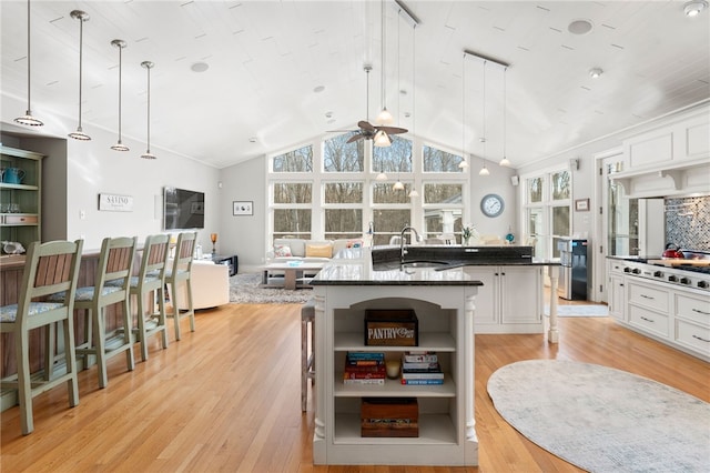 kitchen with sink, a breakfast bar area, hanging light fixtures, an island with sink, and white cabinets