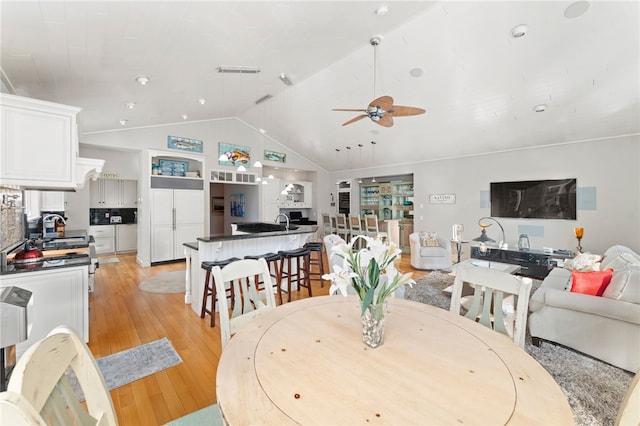 dining space featuring sink, vaulted ceiling, ceiling fan, and light wood-type flooring