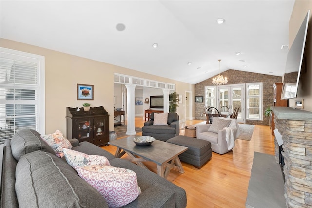 living room with ornate columns, lofted ceiling, a notable chandelier, and light hardwood / wood-style floors