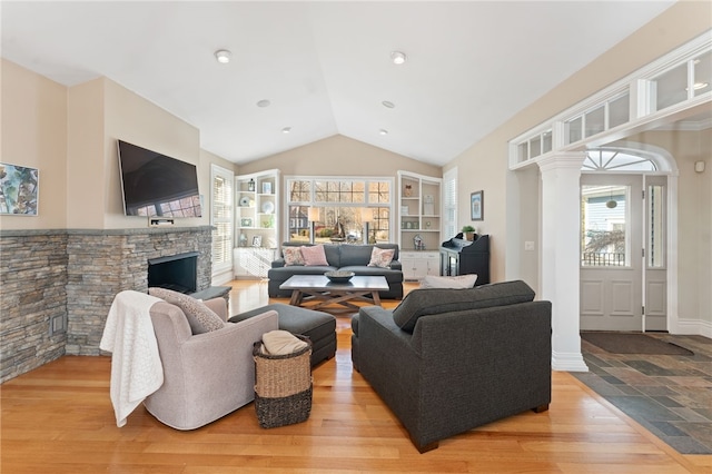 living room featuring ornate columns, lofted ceiling, a fireplace, and light wood-type flooring