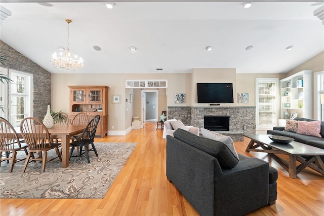 living room with a notable chandelier, a stone fireplace, vaulted ceiling, and light wood-type flooring