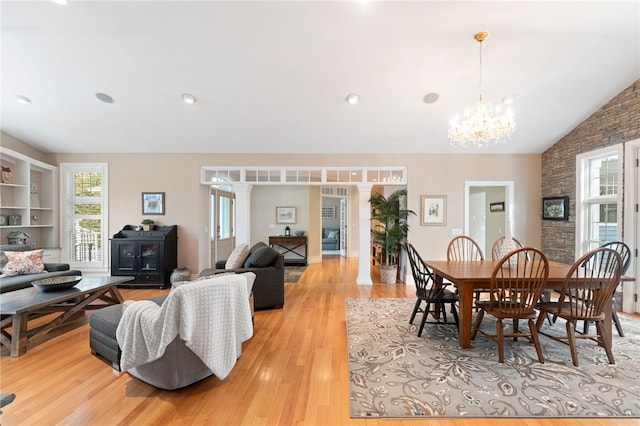 dining room featuring lofted ceiling, ornate columns, an inviting chandelier, and light wood-type flooring