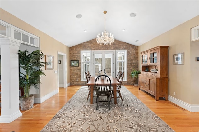 dining area featuring french doors, lofted ceiling, light hardwood / wood-style flooring, a notable chandelier, and brick wall