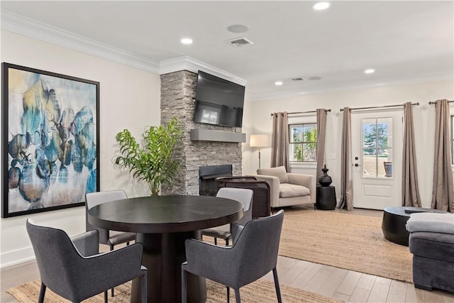 dining space with ornamental molding, a stone fireplace, and light wood-type flooring