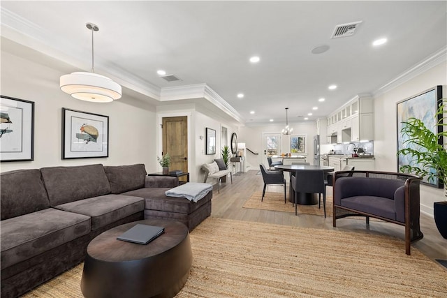 living room with ornamental molding, a chandelier, and light hardwood / wood-style floors