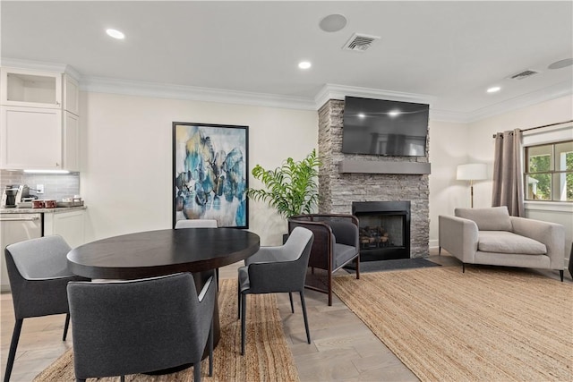 dining area with crown molding, a stone fireplace, and light wood-type flooring