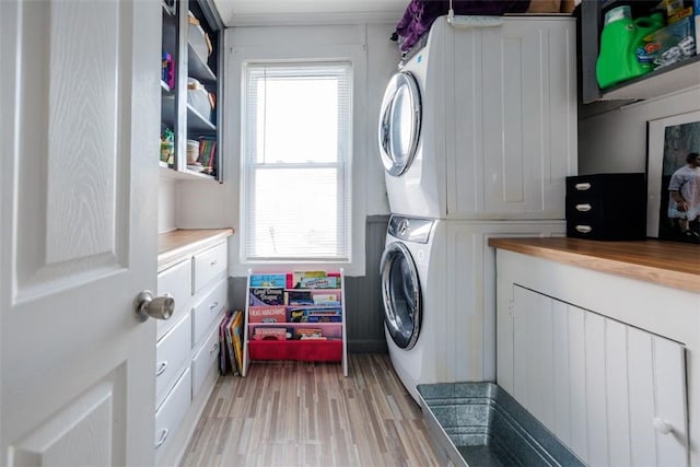 laundry room with cabinets, a healthy amount of sunlight, stacked washer / drying machine, and light wood-type flooring