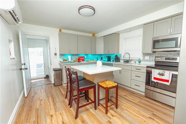 kitchen with a wall mounted AC, a kitchen bar, a center island, stainless steel appliances, and light hardwood / wood-style flooring