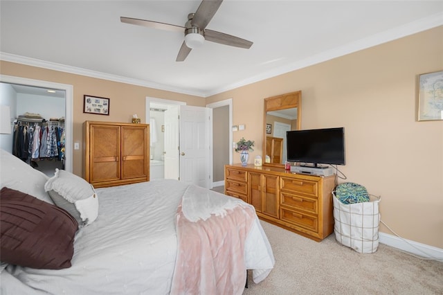 bedroom featuring connected bathroom, a walk in closet, light colored carpet, ornamental molding, and ceiling fan