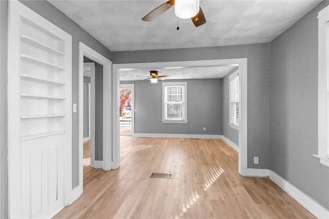 unfurnished living room with ceiling fan, light wood-type flooring, and built in shelves