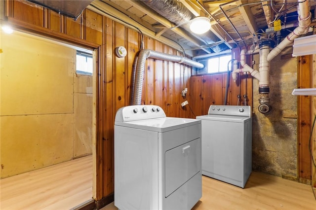 clothes washing area with independent washer and dryer, wooden walls, and light hardwood / wood-style floors