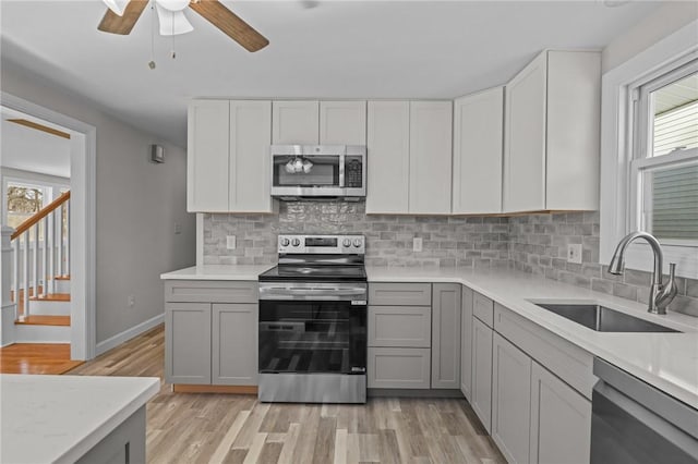 kitchen with gray cabinetry, sink, light hardwood / wood-style floors, and appliances with stainless steel finishes