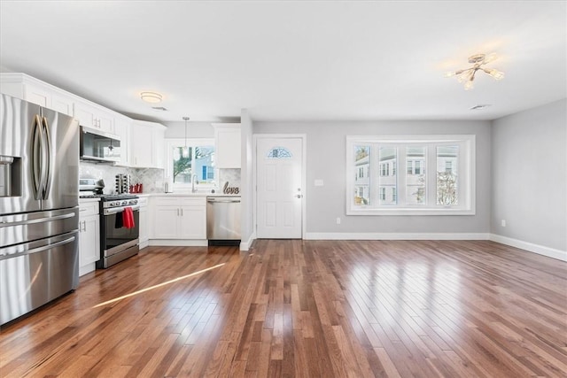 kitchen with hardwood / wood-style flooring, hanging light fixtures, stainless steel appliances, tasteful backsplash, and white cabinets