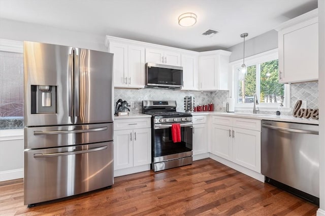 kitchen featuring pendant lighting, sink, white cabinets, stainless steel appliances, and dark wood-type flooring