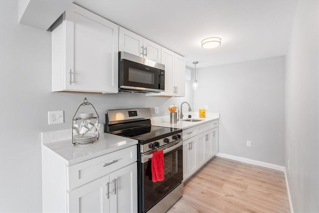 kitchen featuring sink, white cabinetry, hanging light fixtures, stainless steel appliances, and light hardwood / wood-style floors