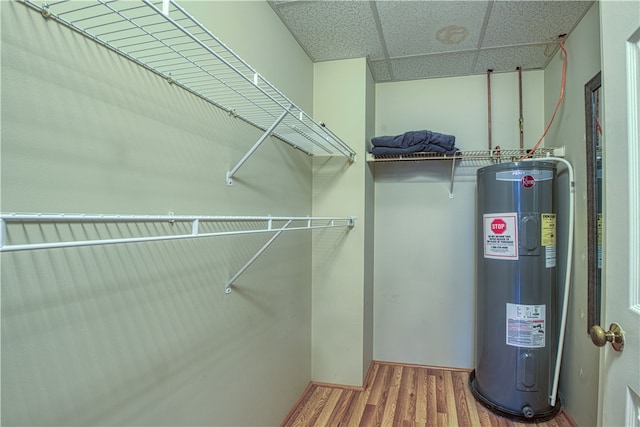 walk in closet with hardwood / wood-style flooring, electric water heater, and a drop ceiling