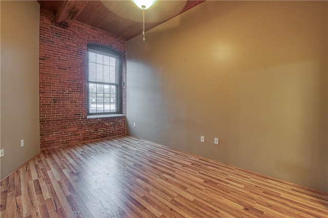 unfurnished room with wood ceiling, light hardwood / wood-style flooring, beamed ceiling, and brick wall