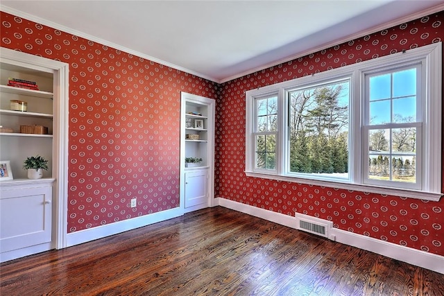 empty room featuring wallpapered walls, baseboards, visible vents, dark wood-style flooring, and crown molding