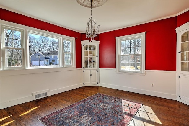 unfurnished dining area with crown molding, visible vents, wainscoting, wood finished floors, and baseboards