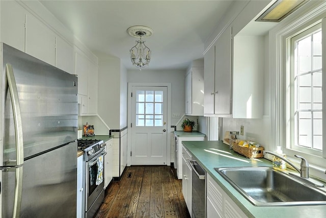 kitchen with white cabinets, dark wood-style floors, appliances with stainless steel finishes, decorative light fixtures, and a sink