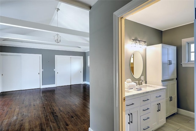 bathroom with vaulted ceiling with beams, wood finished floors, vanity, and baseboards