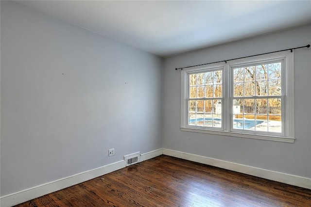 unfurnished room with dark wood-style flooring, visible vents, and baseboards