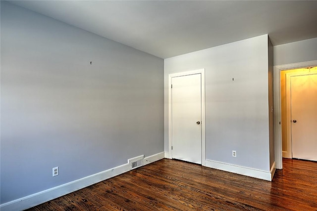 empty room with dark wood finished floors, visible vents, and baseboards