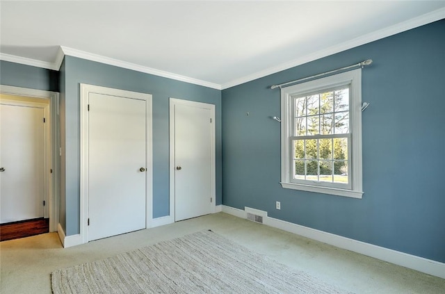 unfurnished bedroom with carpet floors, visible vents, baseboards, ornamental molding, and two closets