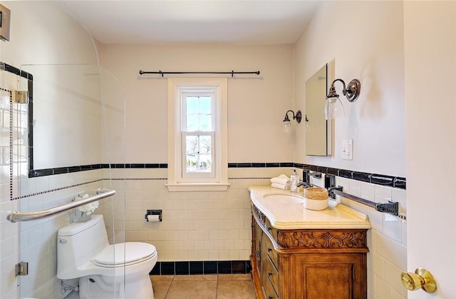 bathroom featuring toilet, a wainscoted wall, tile patterned floors, vanity, and tile walls