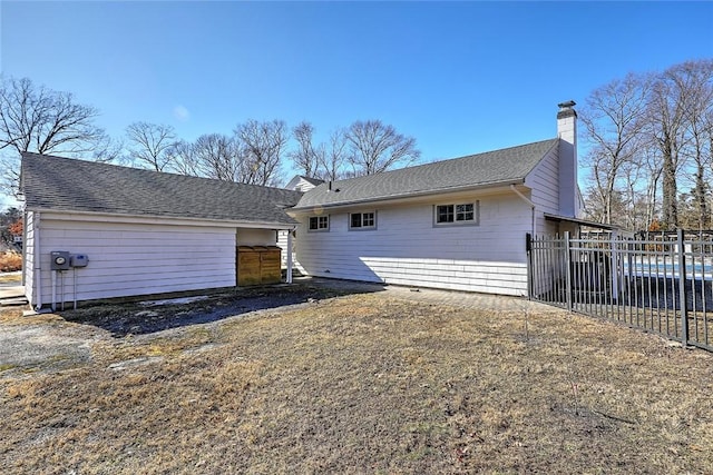 back of house featuring a shingled roof, fence, and a chimney