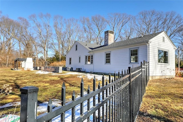 exterior space with an outbuilding, central AC, a shingled roof, fence, and a chimney