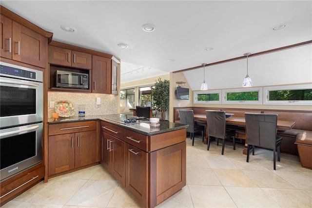 kitchen with light tile patterned floors, appliances with stainless steel finishes, hanging light fixtures, tasteful backsplash, and dark stone counters