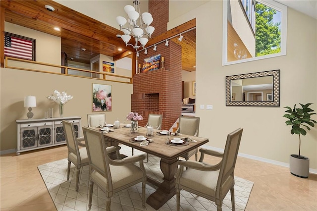 tiled dining room featuring rail lighting, an inviting chandelier, a high ceiling, a fireplace, and wooden ceiling