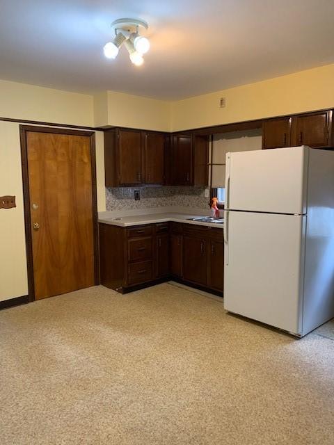 kitchen featuring decorative backsplash, dark brown cabinetry, sink, and white fridge