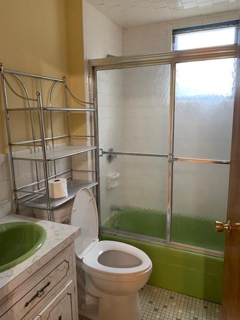 full bathroom with tile patterned flooring, vanity, bath / shower combo with glass door, and toilet