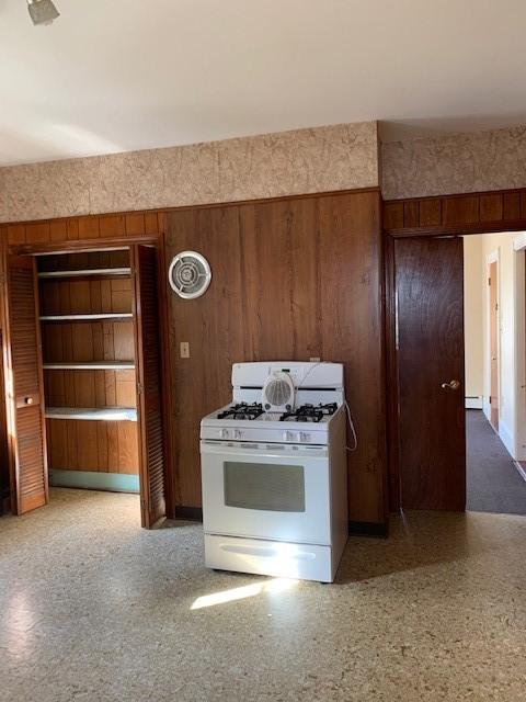 kitchen featuring a baseboard radiator, wooden walls, and white gas range oven